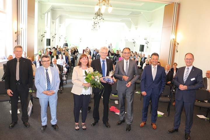 Eine Gruppe von Menschen steht in einem Raum, während ein Mann einen Blumenstrauß hält.