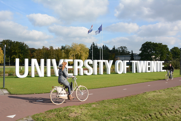 Zwei Personen fahren mit Fahrrädern am Schild der Universität Twente vorbei.