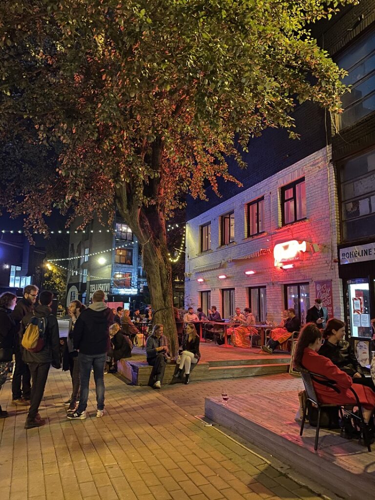 Menschen sitzen auf Bänken in einem Stadtplatz.