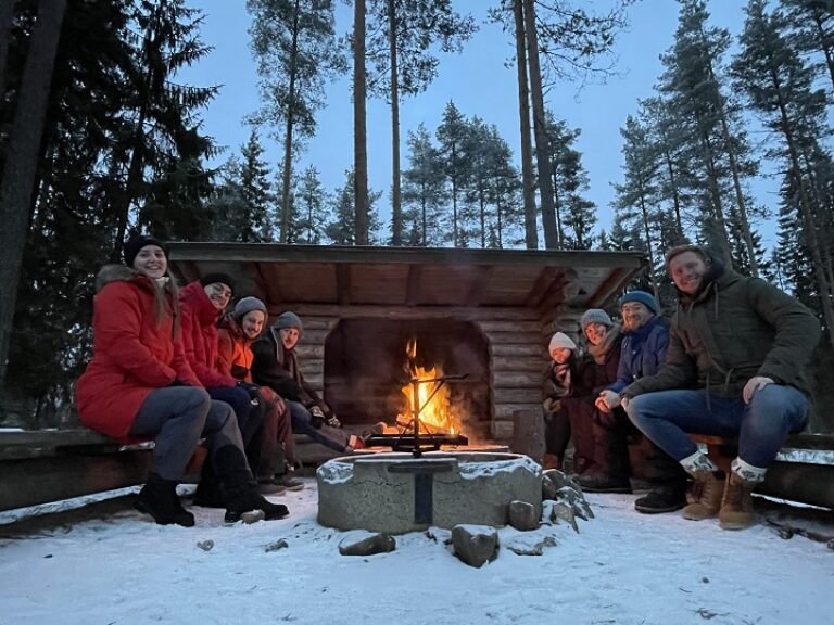 Eine Gruppe Menschen sitzt im Schnee um ein Feuer herum.
