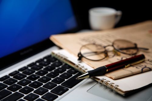Ein Schreibtisch mit einem Notizbuch, einem Stift, einer Brille und einem Laptop.