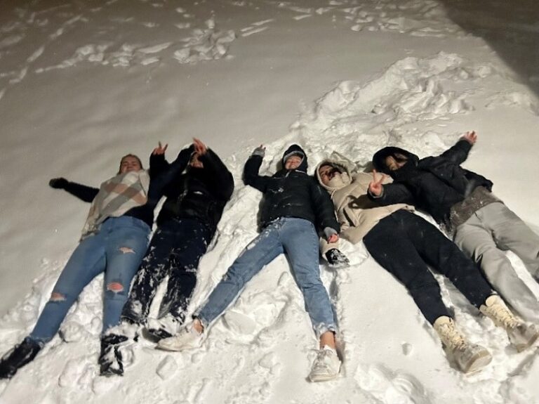 Menschen liegen im Schnee und recken ihre Arme in die Höhe.