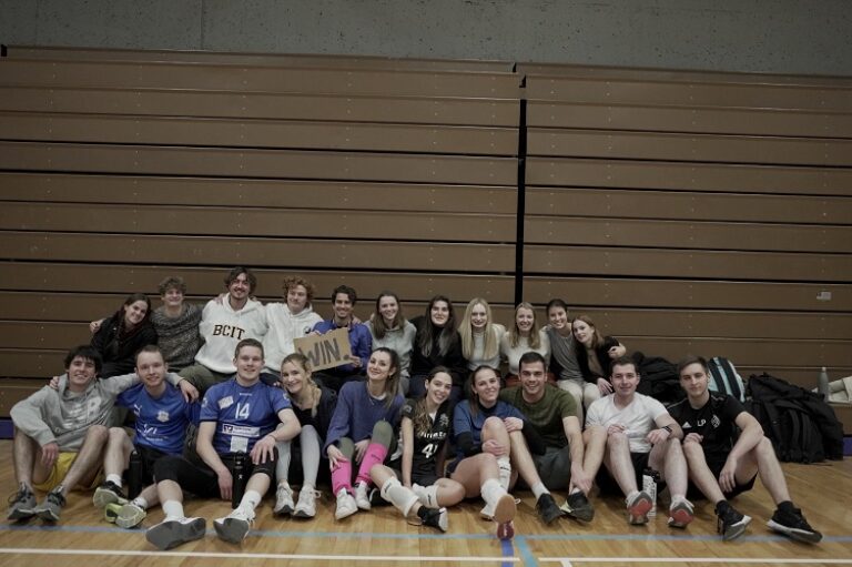 Eine Gruppe von Menschen sitzt auf dem Boden in einer Sporthalle.
