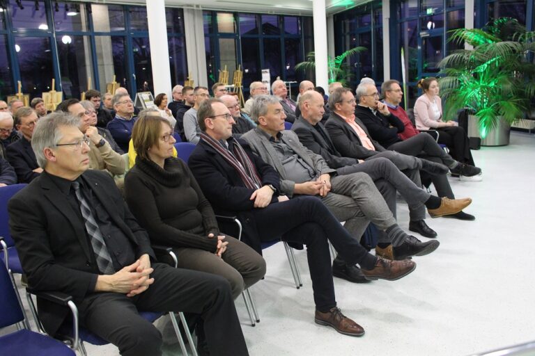 Eine große Gruppe von Menschen sitzt in einem Raum auf Stühlen.