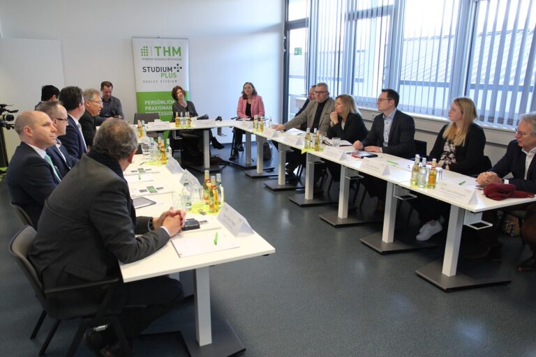 Eine Gruppe von Menschen sitzt an langen Tischen in einem Raum.