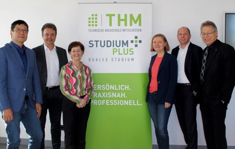 Eine Gruppe von Menschen steht vor einem Schild. Das Bild zeigt das THM und StudiumPlus Logo.