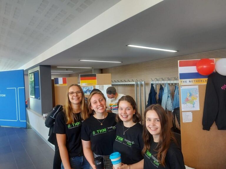 Vier junge Frauen in schwarzen Shirts stehen in einem Flur.