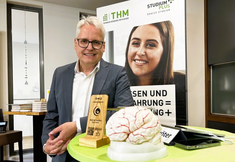 Eine Person mit Brille steht neben einem Tisch mit einem Gehirn.