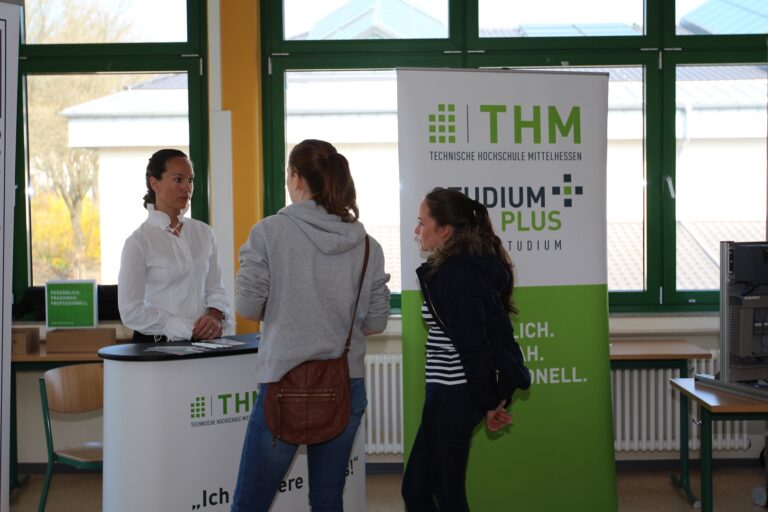 Menschen stehen um einen Tisch herum, auf dem ein Schild mit der Aufschrift "THM" liegt.