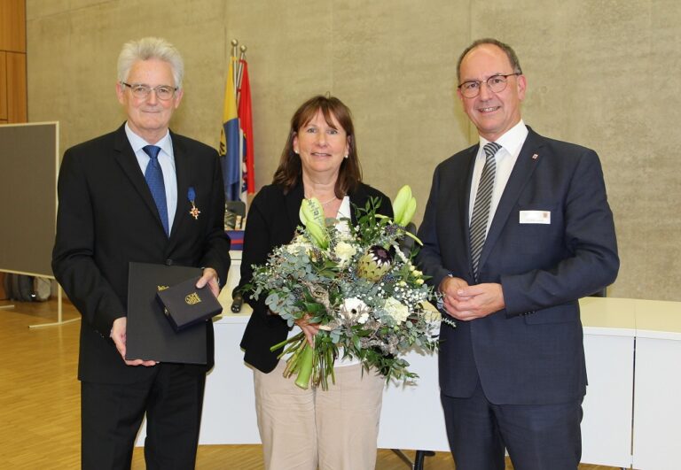 Drei Personen in Anzügen halten Blumen und stehen nebeneinander.
