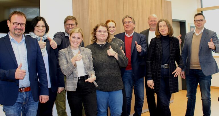 Eine Gruppe von Personen steht in einem Raum und zeigt Daumen hoch.
