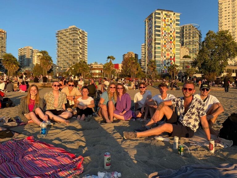 Eine Gruppe von Menschen sitzt am Strand vor Gebäuden.