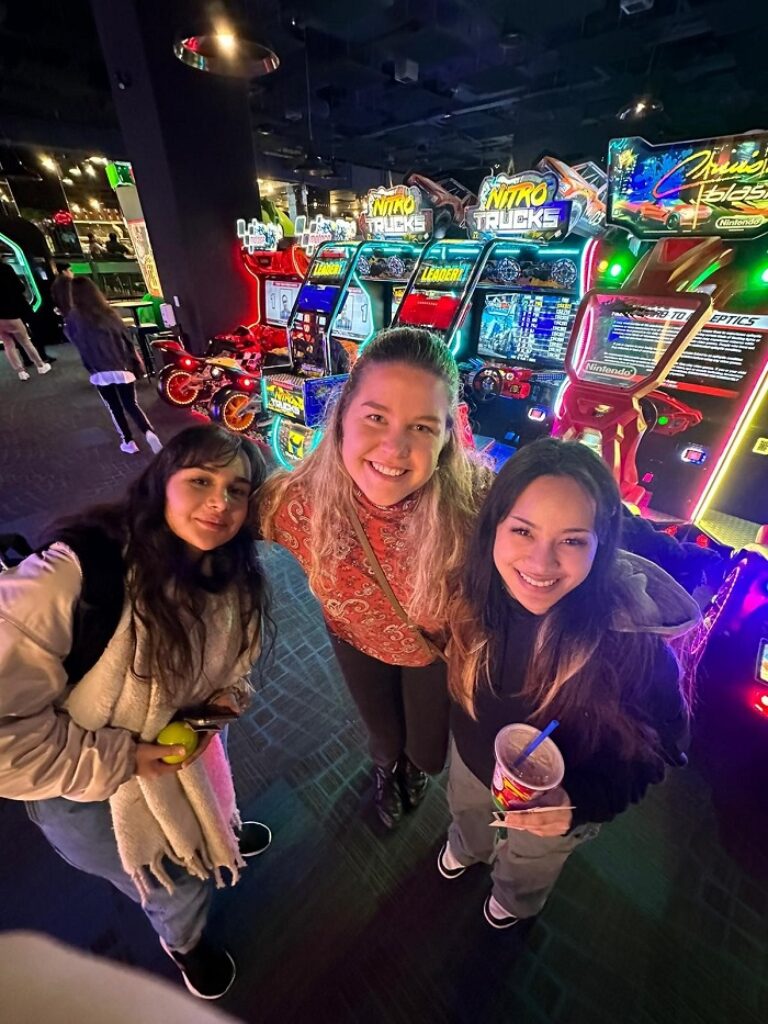Drei Mädchen lächeln vor Spielautomaten für ein Foto.