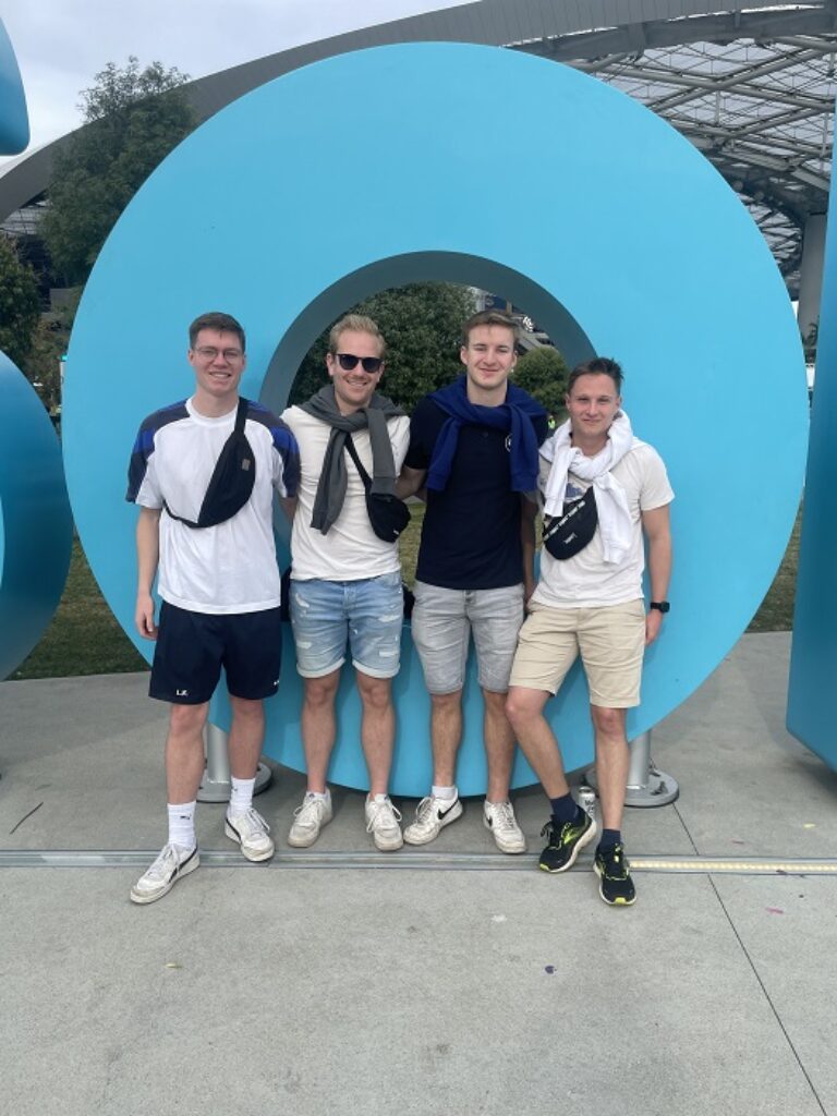 Vier junge Männer stehen vor einem großen Schild.