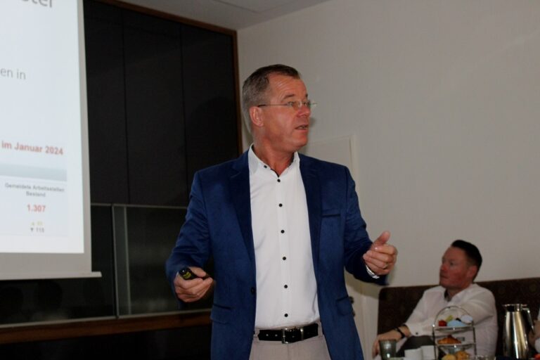 Oliver Klimke präsentiert selbstbewusst in einem Anzug vor dem interessierten Publikum.