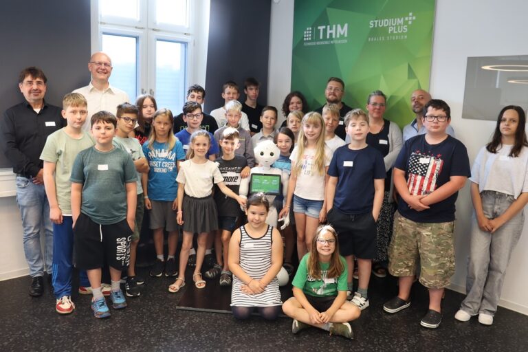 23 Kinder stehen gemeinsam mit den Organisatoren um den Roboter Pepper herum.
