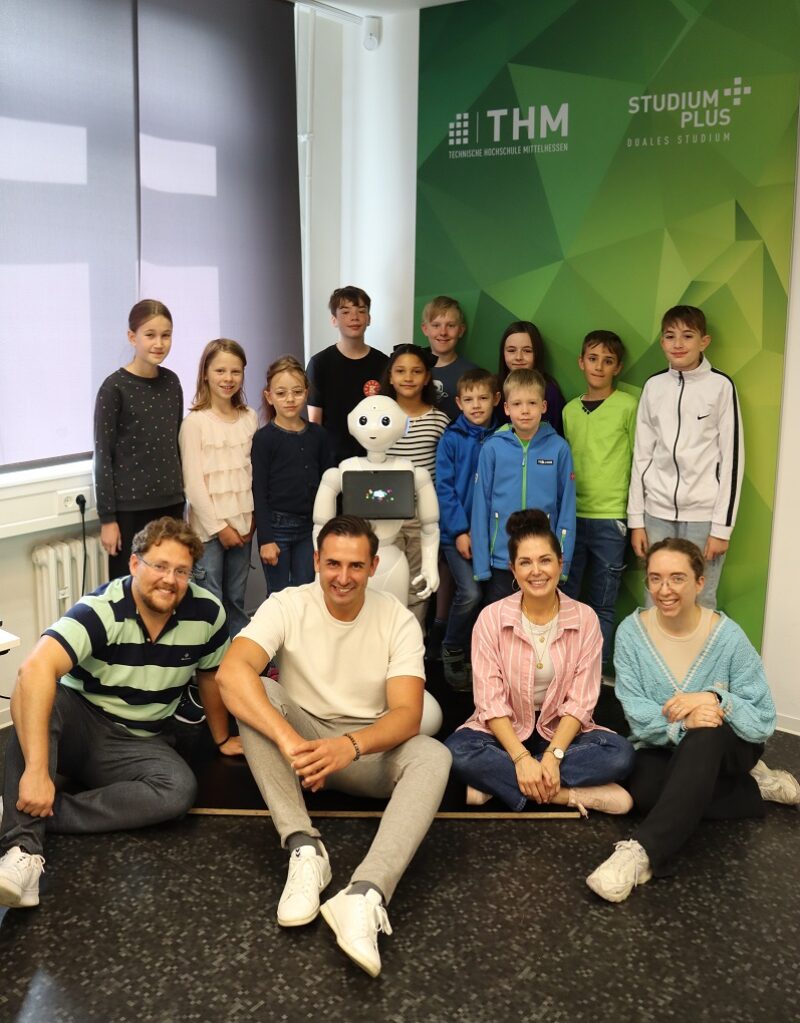 Mitarbeitende von StudiumPlus gemeinsam mit den teilnehmenden Kindern und Pepper